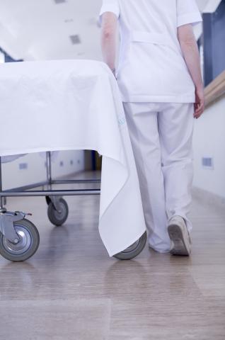 image Enfermera de espaldas empujando una camilla vacía por el pasillo de un hospital