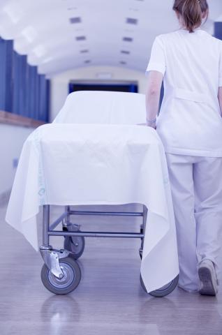 image Enfermera de espaldas empujando una camilla vacía por el pasillo de un hospital