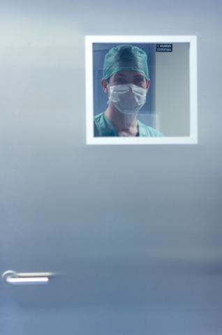 image Un médico con mascarilla mirando por la ventana de la puerta de un quirófano
